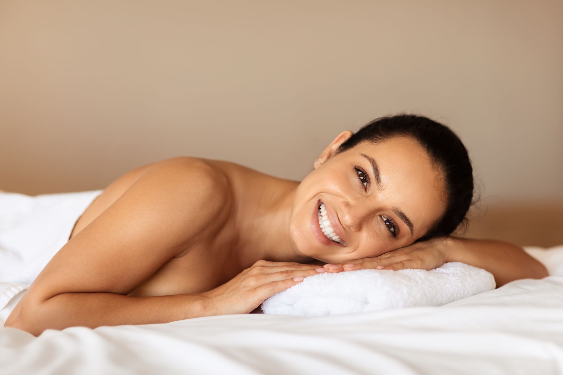 Una mujer está acostada en una cama con una toalla en la cabeza y sonriendo.