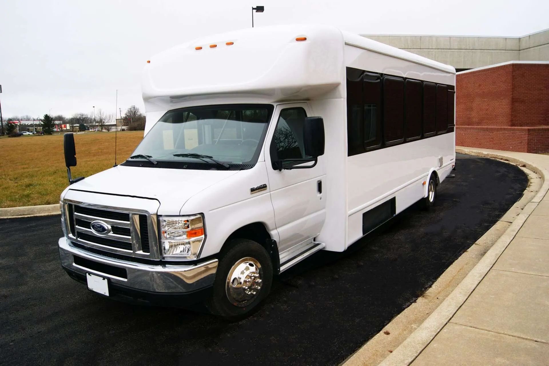 A white bus is parked in a parking lot next to a brick building.