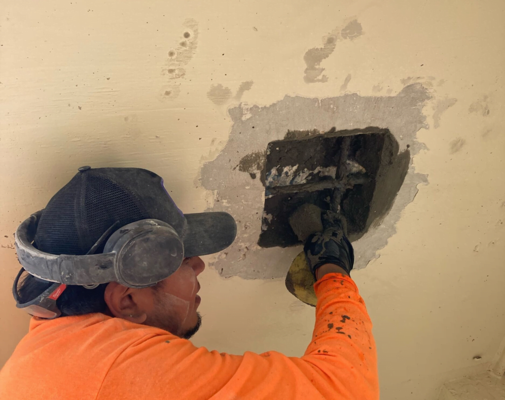 A man wearing headphones and a hat is plastering a wall.