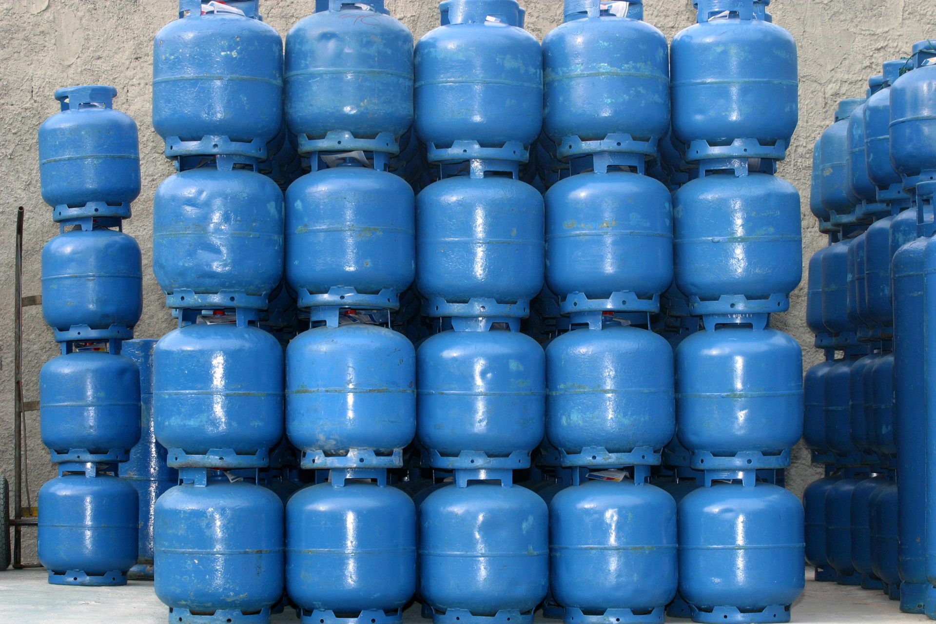 Tanques de propano azules apilados en filas contra un fondo sencillo.