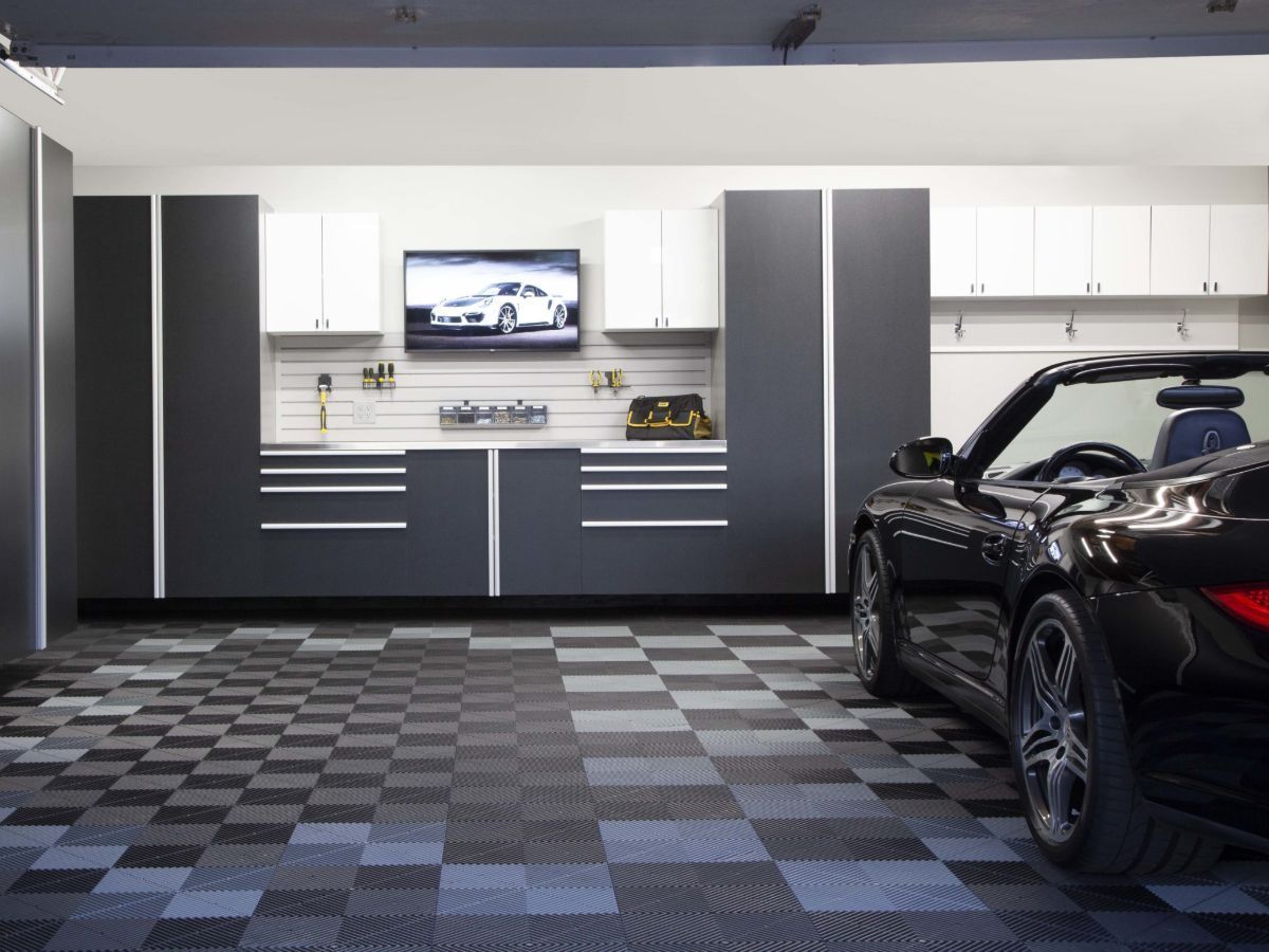 A clean, organized garage with a black sports car. Checkered floor, cabinets, and a TV are visible.