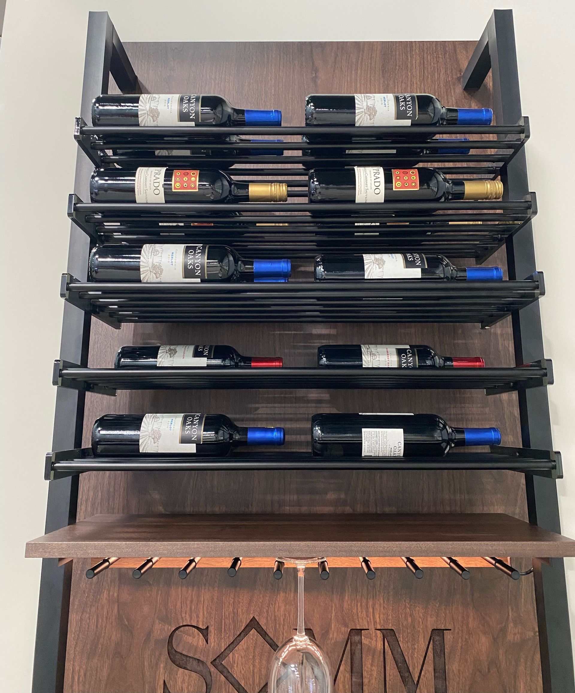 Wine rack on wood backing with metal bars, holding bottles. Includes a stemware rack and the word