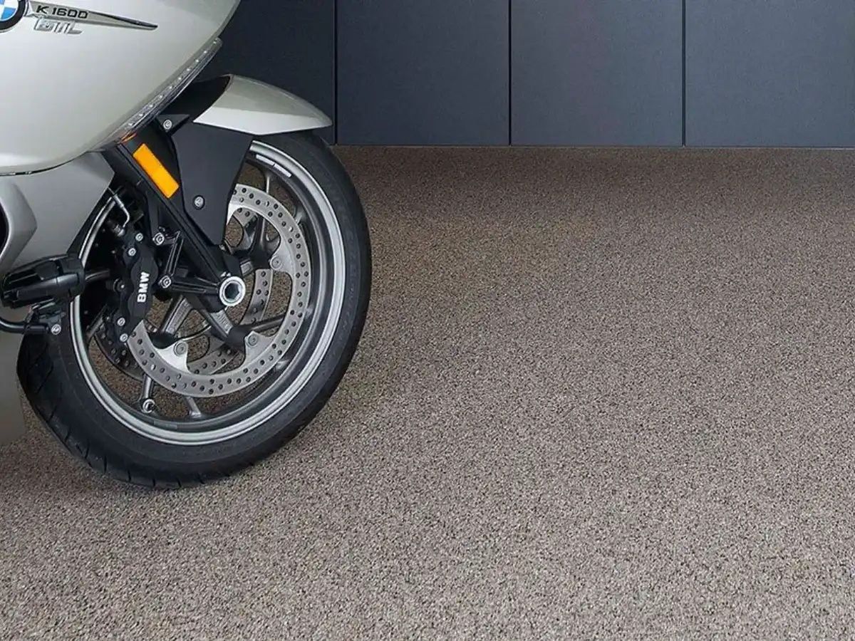 Motorcycle's front wheel on a textured, speckled gray floor; a gray wall in the background.