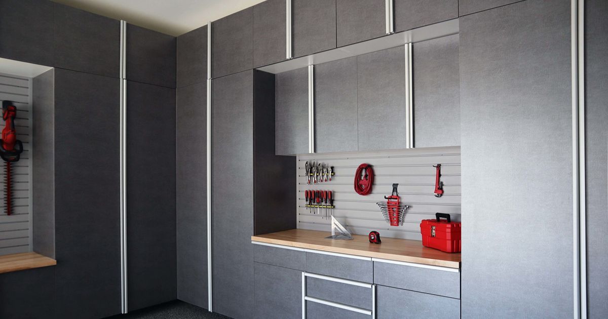 Gray garage storage with cabinets, a workbench, and tools hanging on a slat wall.