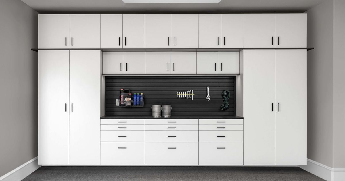 White garage cabinets with black work area and tools against a gray wall.