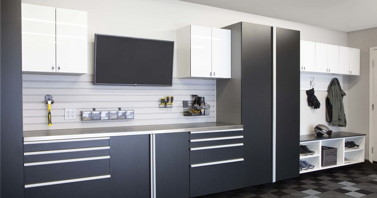 Garage storage system with cabinets, drawers, and a workbench. Gray and white colors. Television mounted.