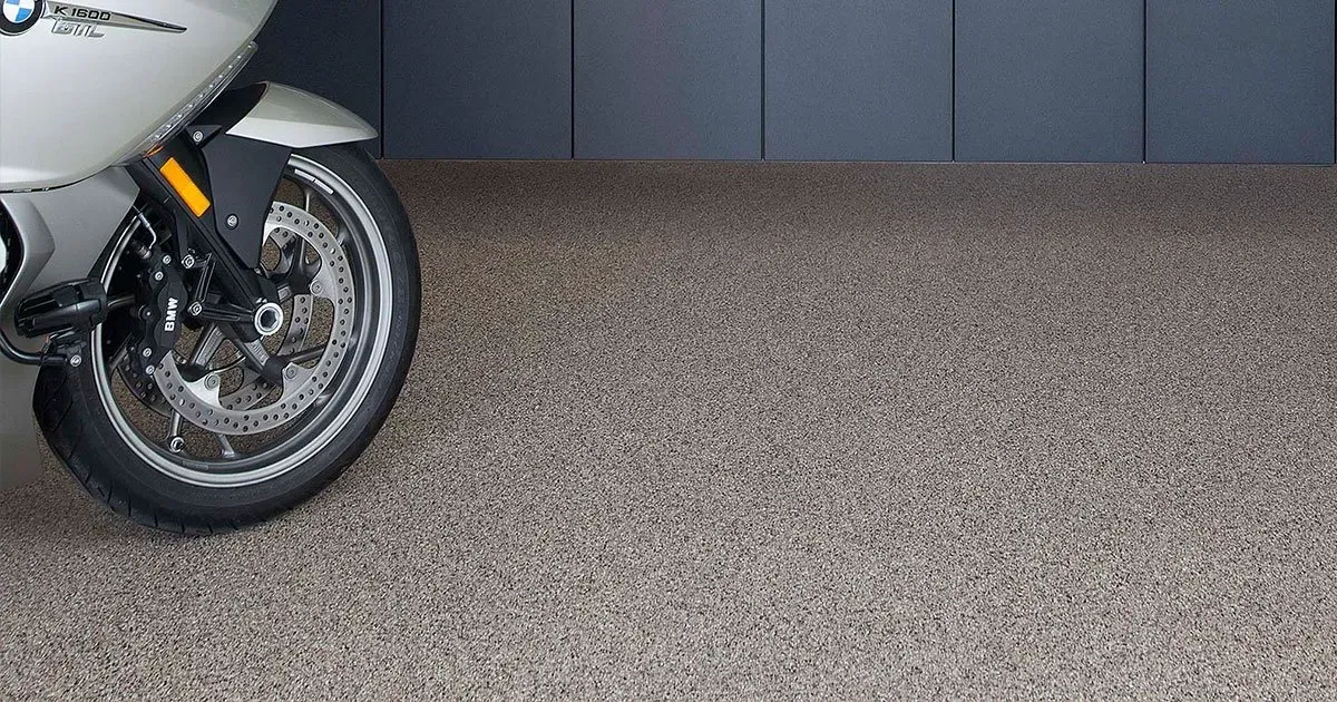 Motorcycle front wheel on a textured, speckled floor in a garage.