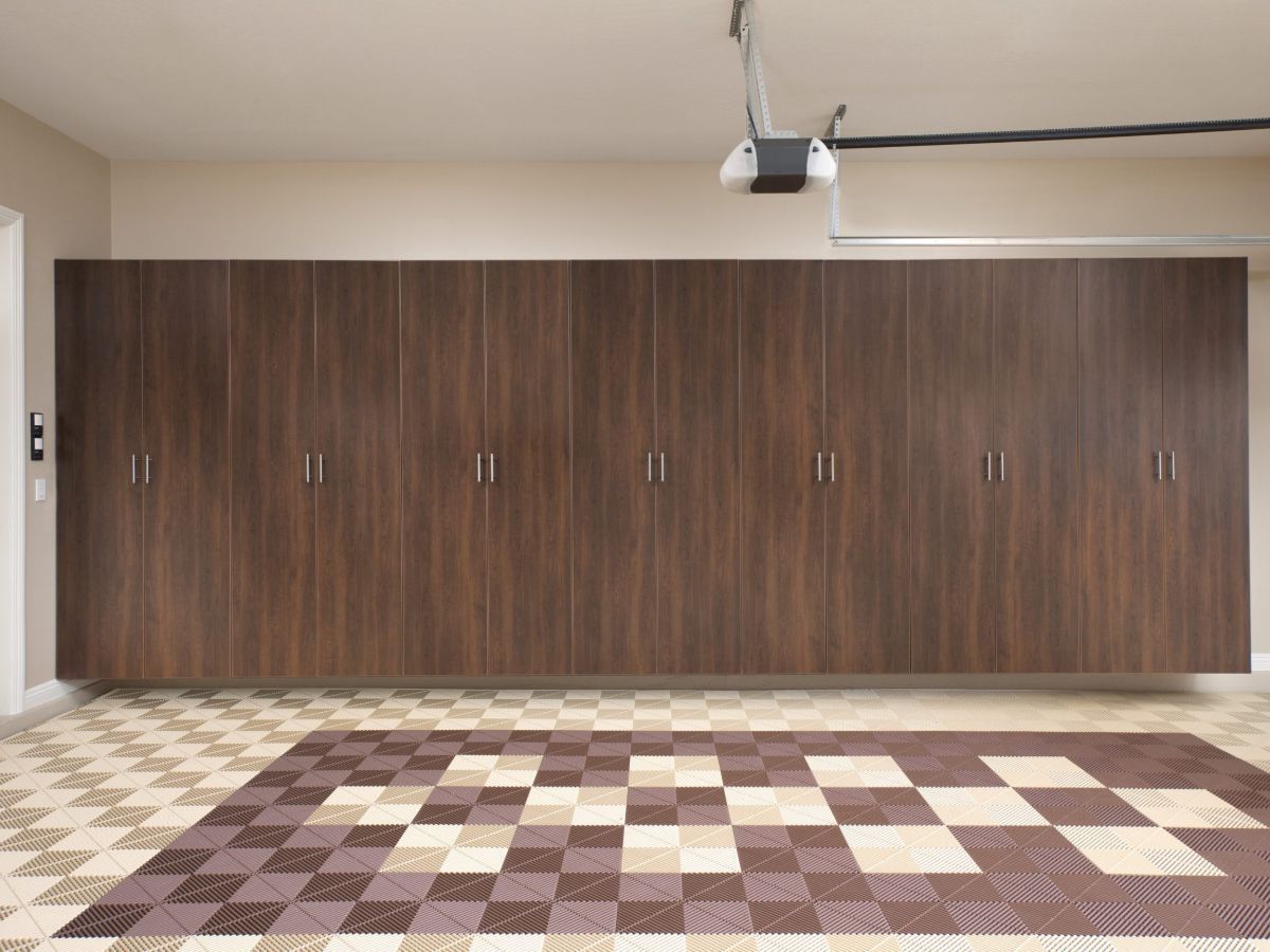 Garage with wall-mounted, dark wood cabinets above a patterned tile floor. A garage door opener hangs from the ceiling.