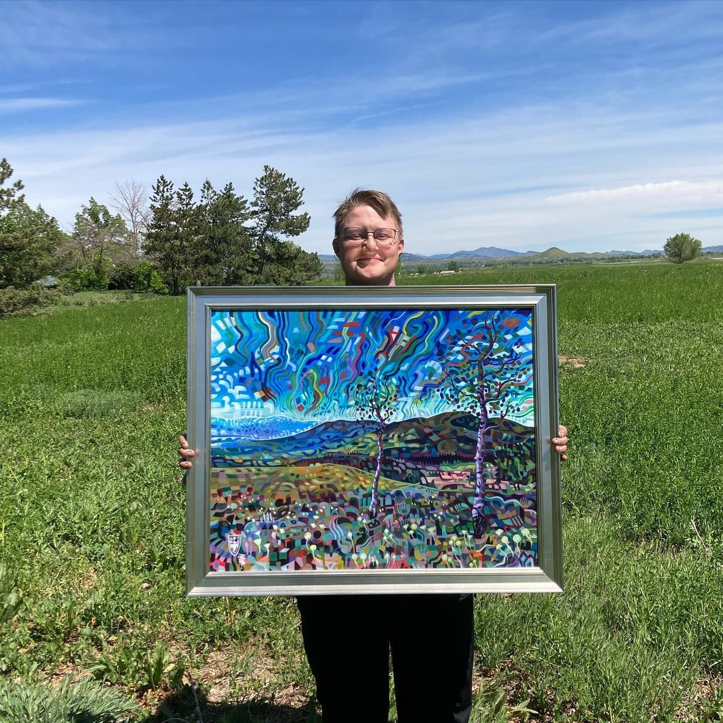 A man is holding a framed painting in a field.