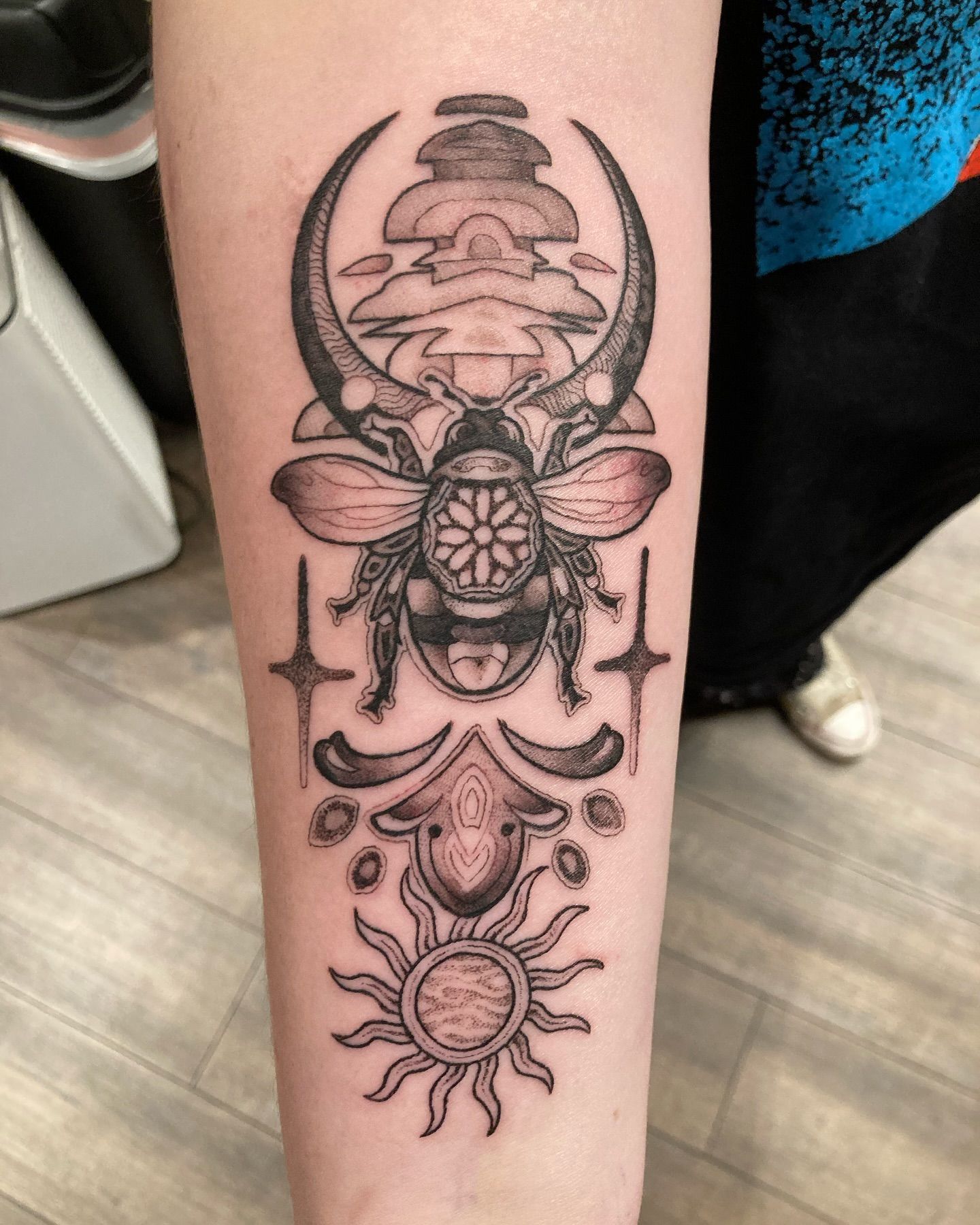A black and white tattoo of a beetle and a sun on a person 's forearm.