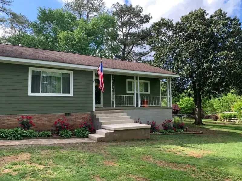 A green house with a red white and blue flag on the porch.