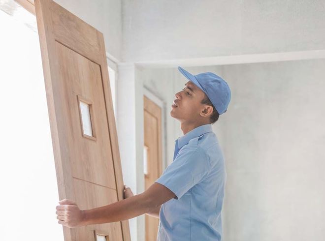 A man in a blue shirt and hat is holding a wooden door.