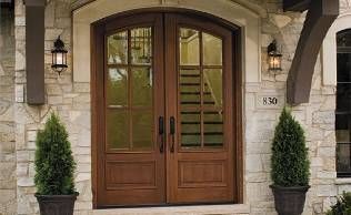 The front door of a house with a wooden door and two potted plants in front of it.