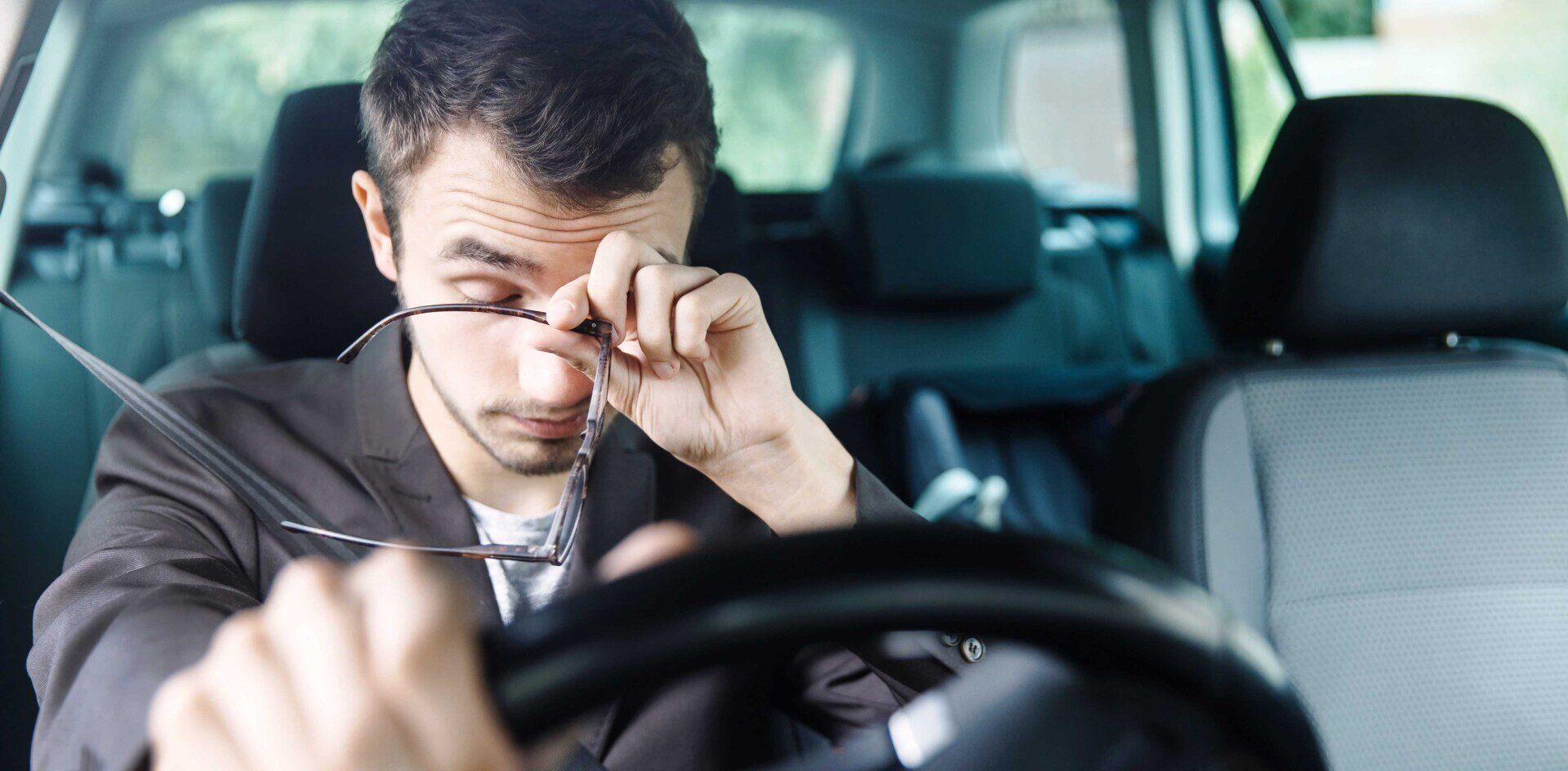 tired driver at the wheel rubbing their eyes holding glasses