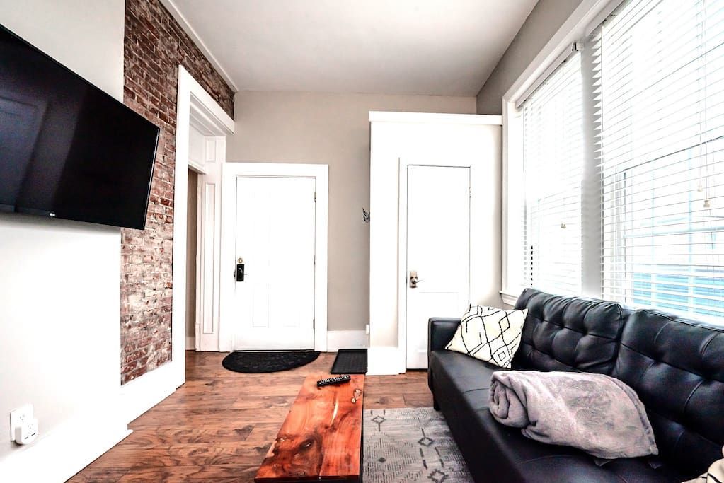 A living room with a black couch and a flat screen tv on the wall.