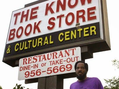 A person wearing a purple shirt stands in front of a sign for