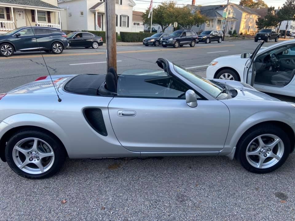 a silver convertible sports car is parked on the side of the road .