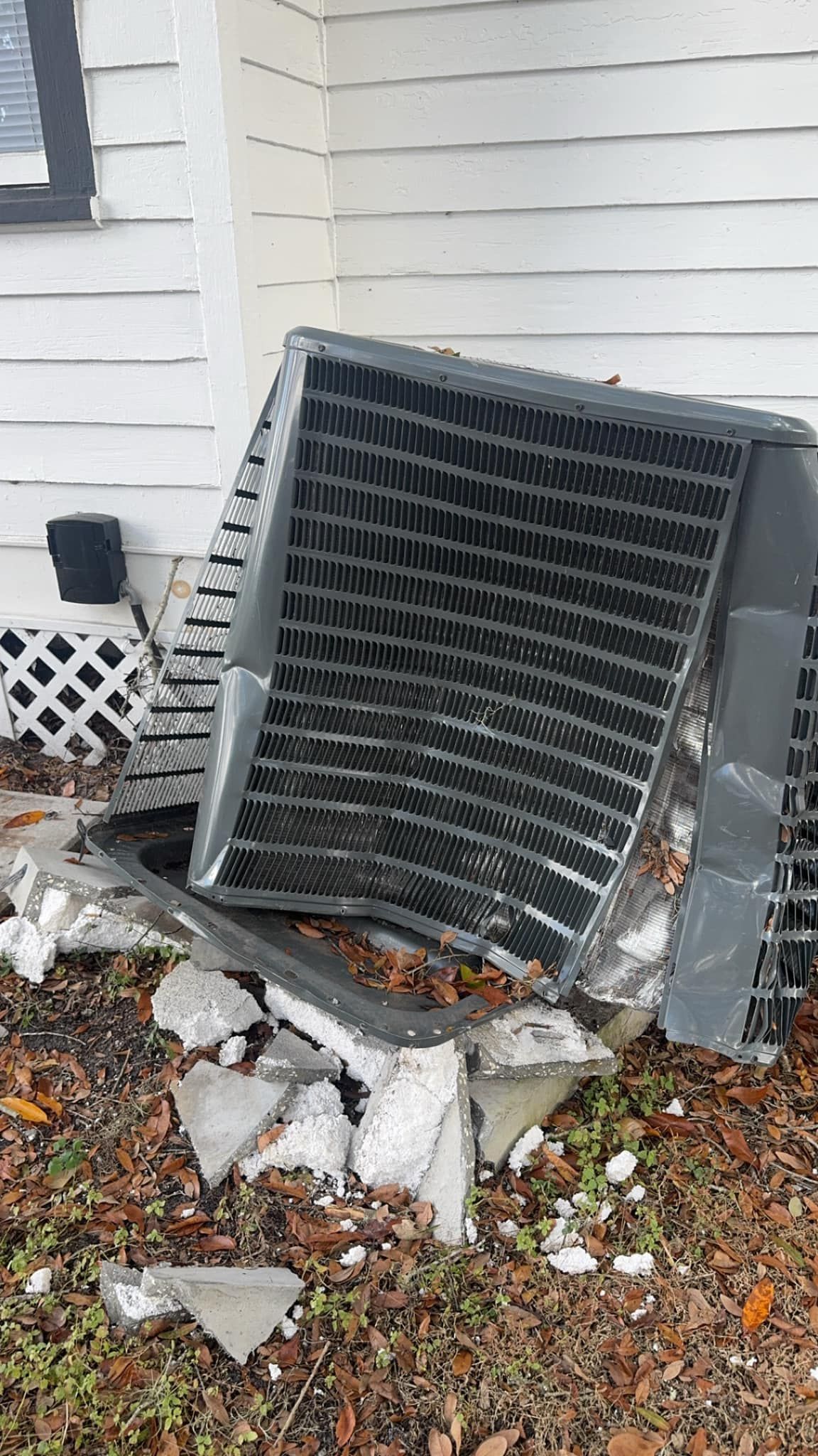 A broken air conditioner is sitting on the ground in front of a house.