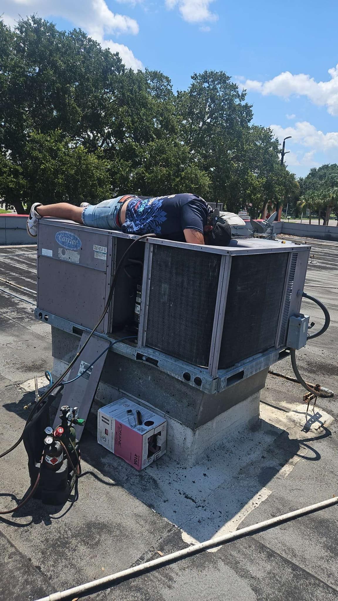 A man is laying on top of an air conditioner on a roof.