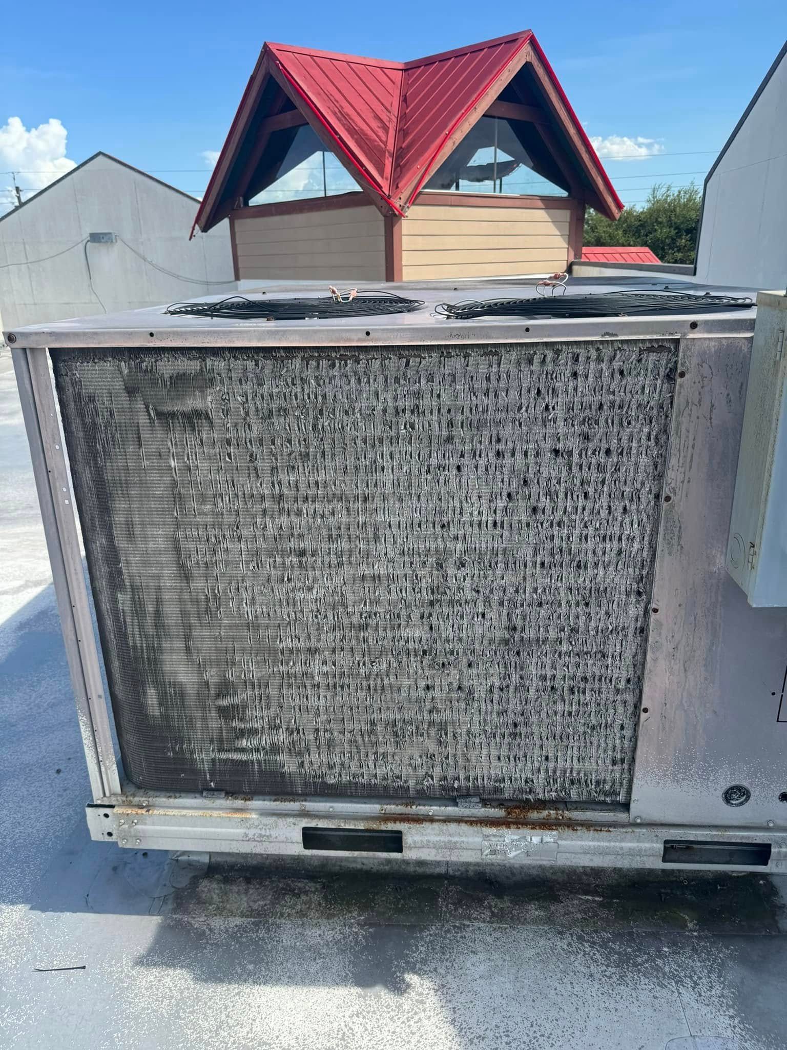 A dirty air conditioner with a red roof is sitting on the ground.