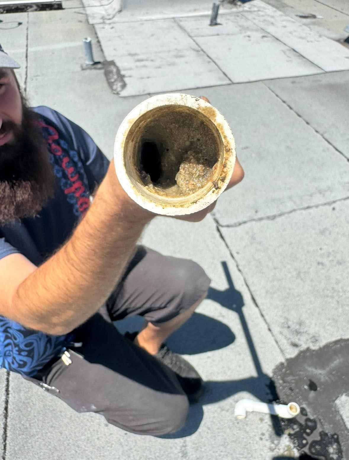 A man with a beard is kneeling down holding a dirty pipe
