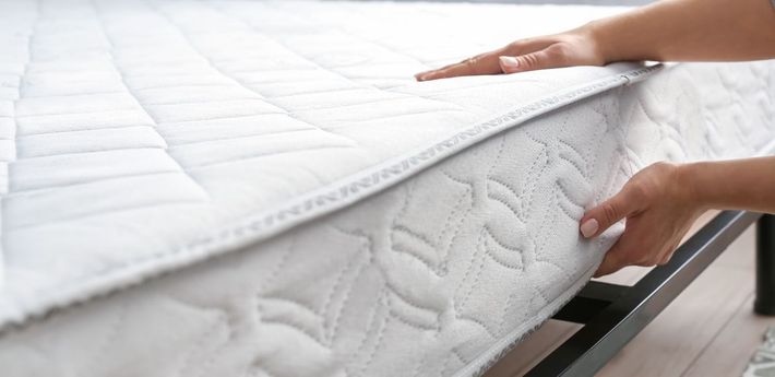 Hands adjusting a white mattress on a metal frame.