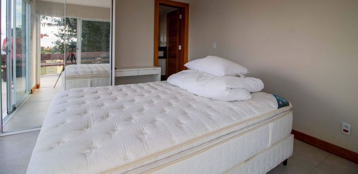 Bedroom with a bed, white mattress, pillows, a desk, and sliding glass doors.