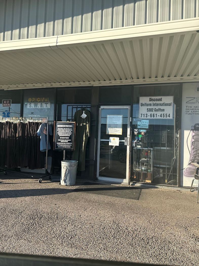 The exterior of a retail storefront with clothing racks, a sign, and a glass door under an awning.
