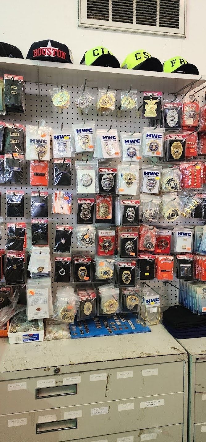 A wall display of badges and patches in plastic sleeves, with a row of colorful hats on a shelf above, inside a shop.