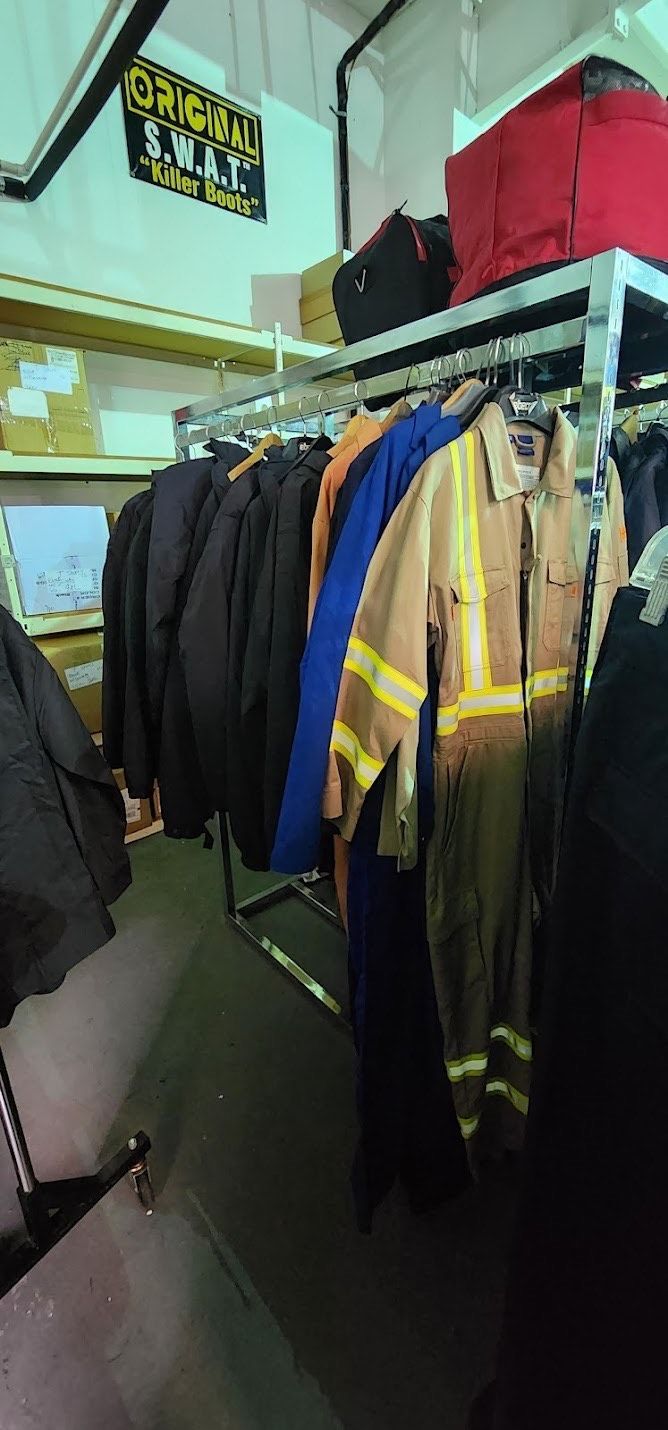 A clothing rack with work jackets and high-visibility coveralls in a storage room with a sign on the wall.
