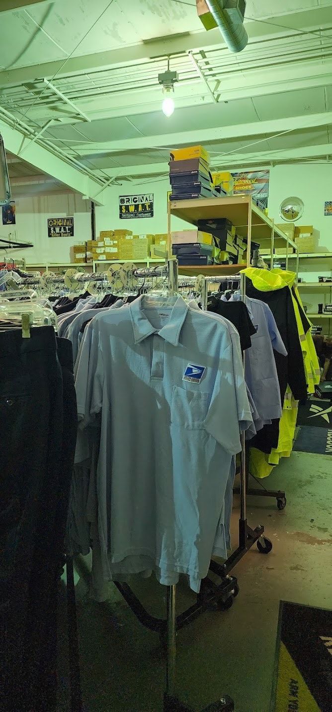 A blue short-sleeved collared shirt hangs on a rack in a retail store with other clothing items in the background.