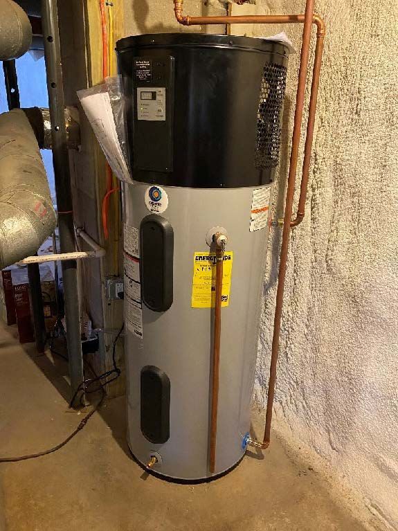 A tall gray and black water heater against a textured wall in a basement. Copper pipes are visible.