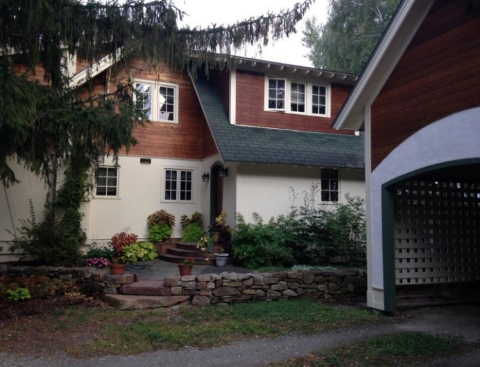 House with red roof and trim, white stucco walls, green roof. Attached garage. Landscaping and stone wall in front.