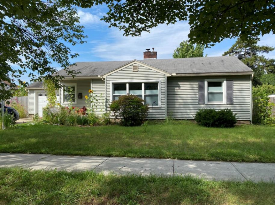 A weathered gray house with overgrown landscaping under a blue sky.