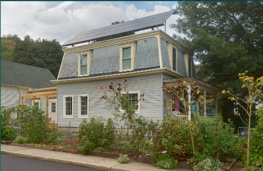 A light blue two-story house with solar panels on the roof and a garden in front.