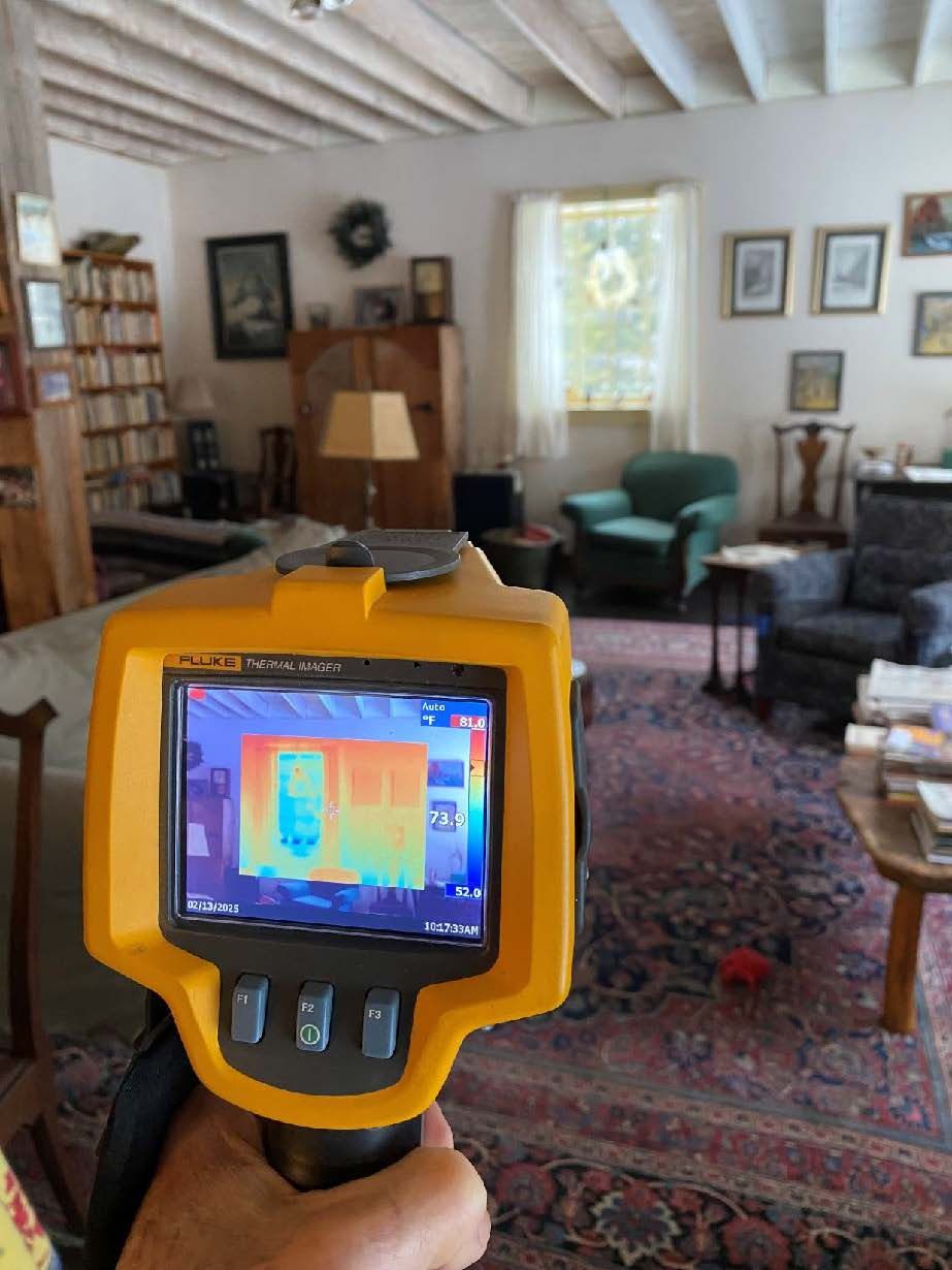 Handheld thermal camera showing a door as red, green, and blue in a room with furniture and rug.