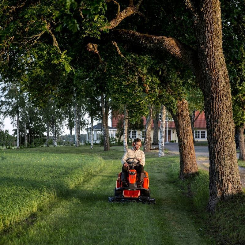A Man Is Riding A Lawn Mower Through A Lush Green Field — Mid Coast Mowers In Taree, NSW