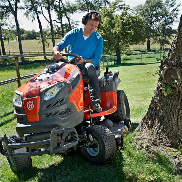 A Man Is Riding a Lawn Mower Next to A Tree — Mid Coast Mowers In Taree, NSW