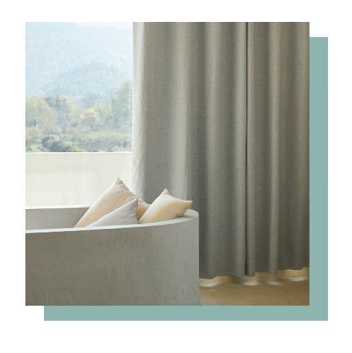 Cozy window seat with cream pillows beside gray curtains, overlooking a soft mountain view