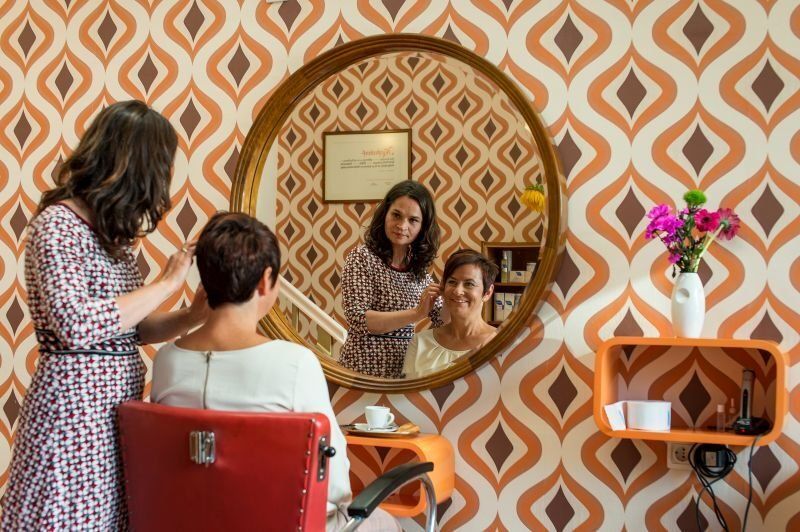 Eine Frau lässt sich in einem Friseursalon vor einem Spiegel die Haare frisieren.