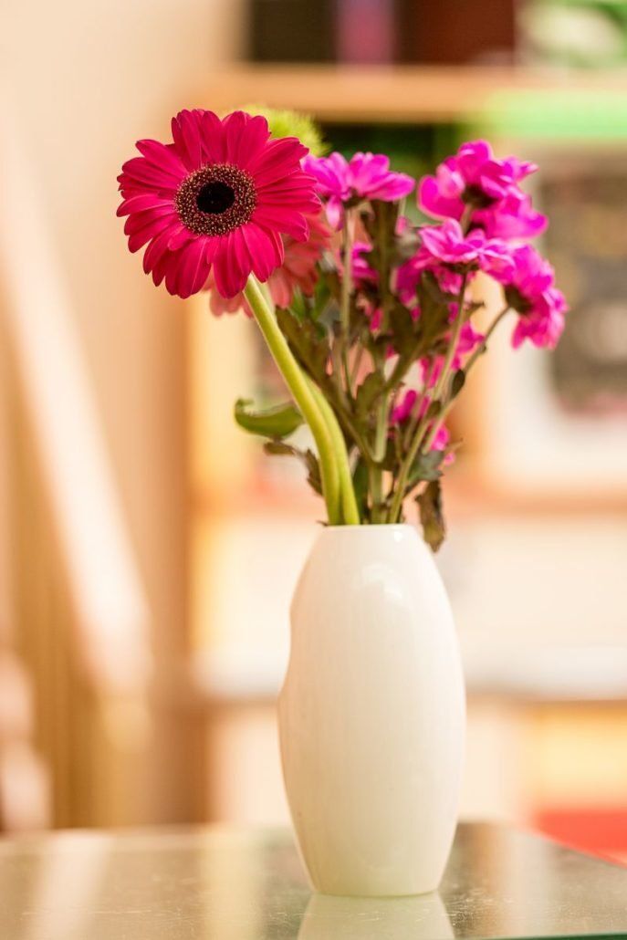 Eine weiße Vase mit rosa Blumen auf einem Tisch