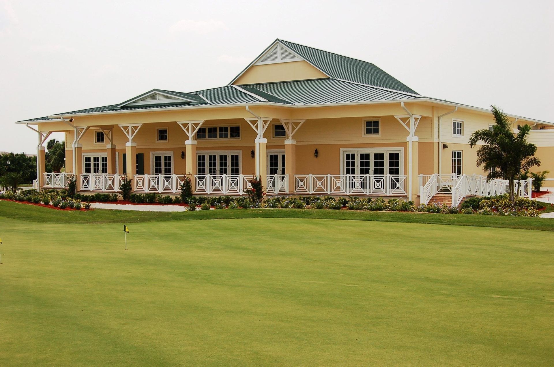 Golf clubhouse with light yellow exterior, white trim, green roof, and manicured lawn.