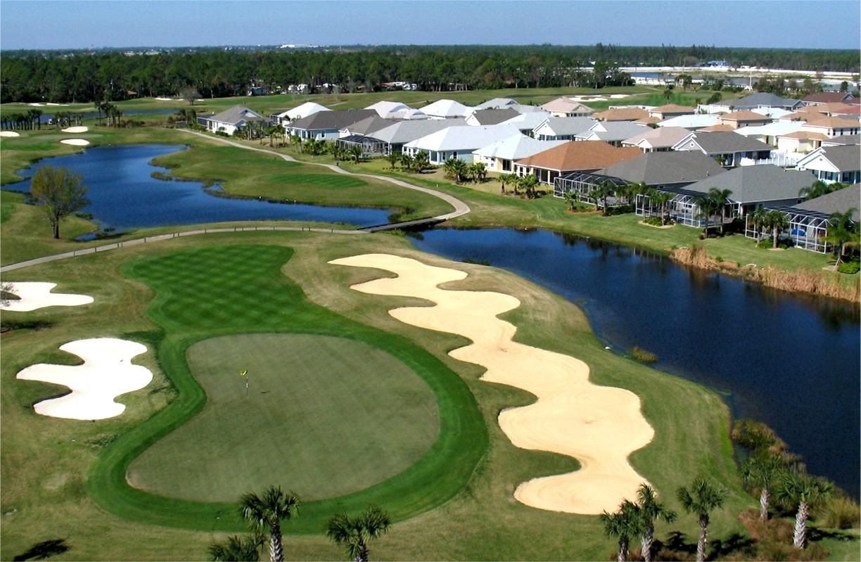 Aerial view of a golf course with green fairway, sand traps, and a blue lake next to residential houses.