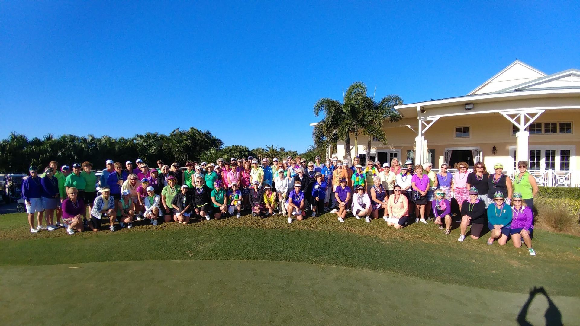 Large group of people in colorful clothes on a golf course, posing for a photo in front of a building.