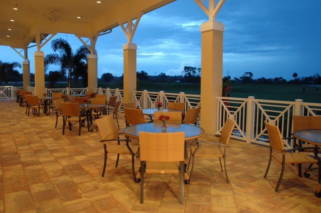 Outdoor patio with tables and chairs, under a covered area, overlooking a golf course at dusk.