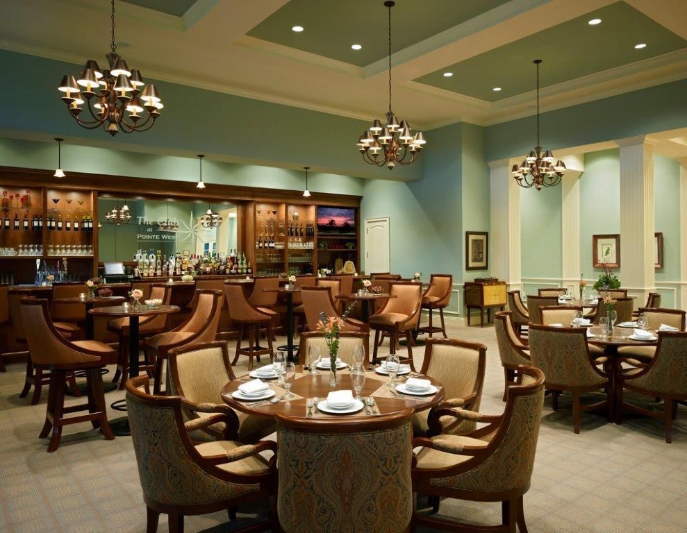 Elegant restaurant interior with round tables, chairs, bar, chandeliers, and teal walls.
