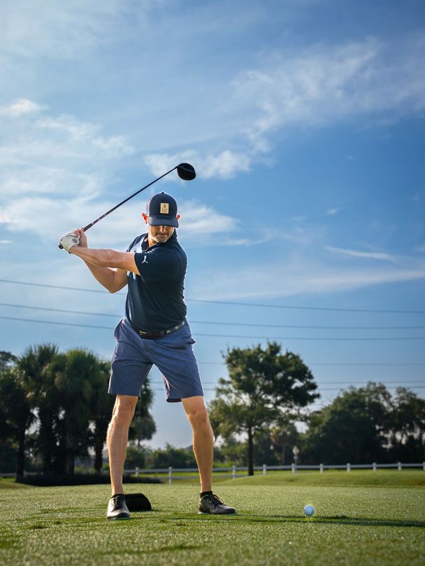 Golfer mid-swing on a golf course under a blue sky.