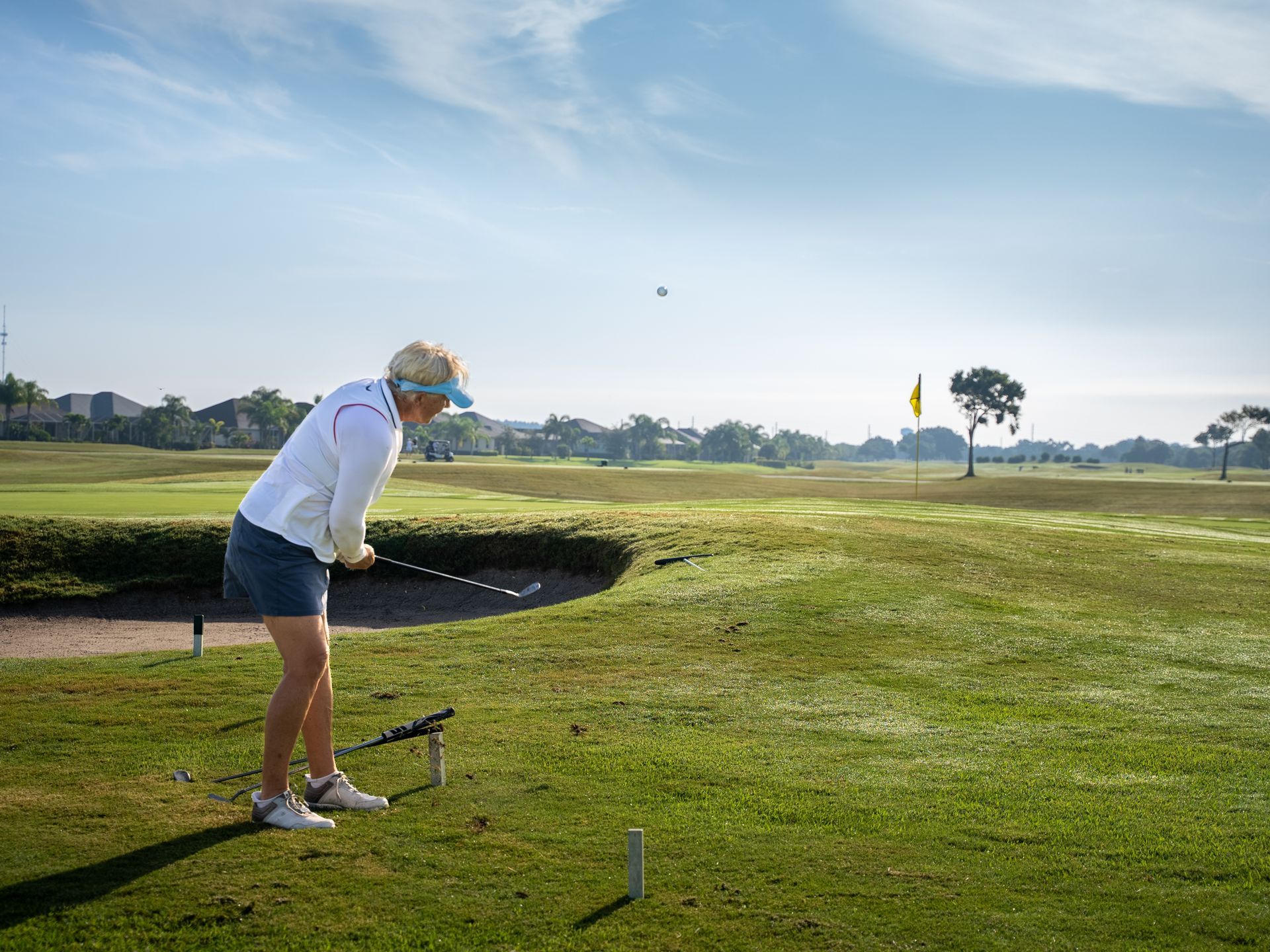 Woman golfing, hitting a ball on a green fairway, sunny day.