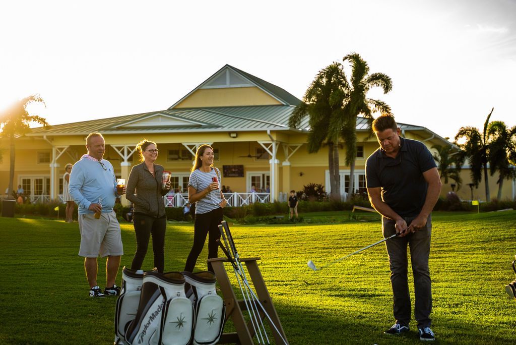 Man golfing, others watch on green lawn near a building. Golden sunlight.