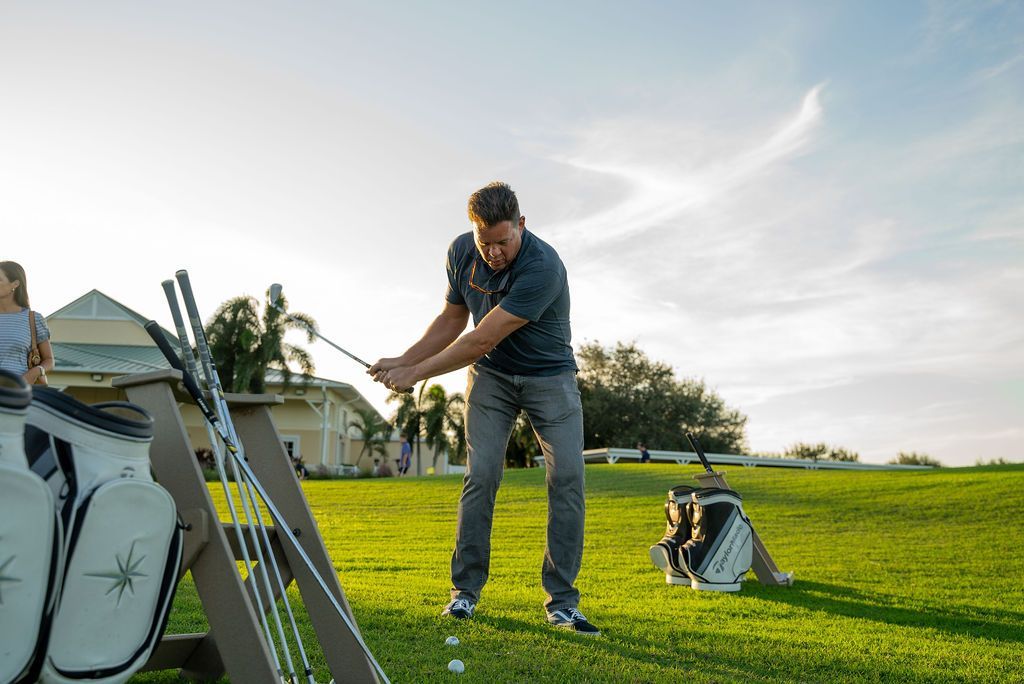Man swings golf club on green, other golf bags and clubs visible.